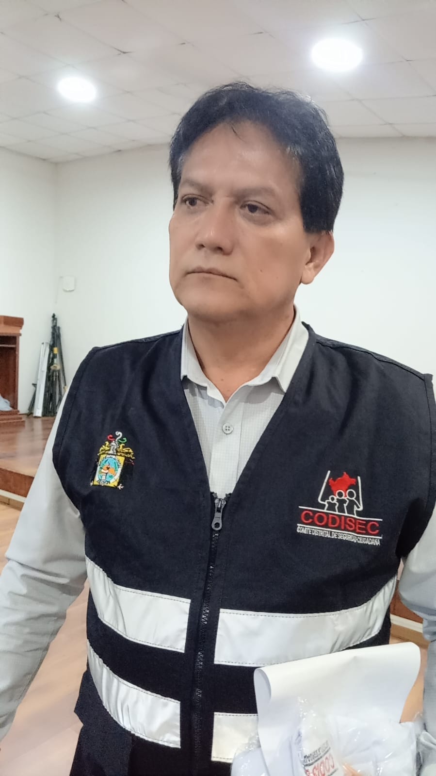 Un hombre de mediana edad con chaleco negro y blanco con logotipos bordados. Está sosteniendo un papel blanco.