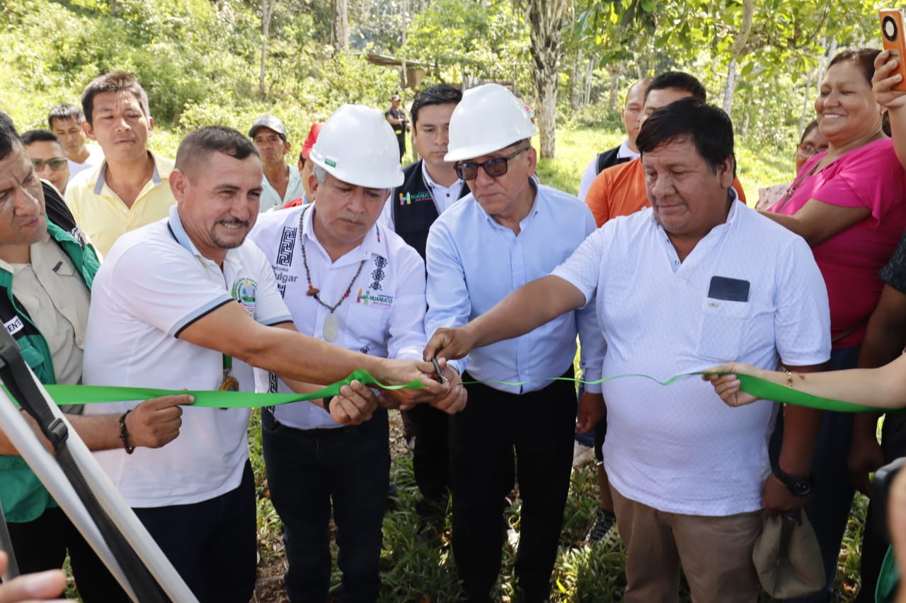 Grupo de personas cortando una cinta verde al aire libre. Hombres con cascos blancos en la ceremonia.